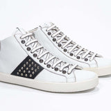 Dreiviertelansicht der Vorderseite von Mid Top weiß und schwarz sneaker. Obermaterial aus Vollleder mit Nieten, einem internen Reißverschluss und einer Vintage-Gummisohle.