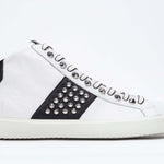 Profilo laterale di mid top bianco e nero sneaker. Tomaia in pelle con borchie, zip interna e suola in gomma bianca.