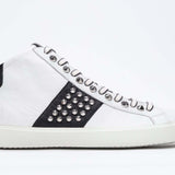 Profilo laterale di mid top bianco e nero sneaker. Tomaia in pelle con borchie, zip interna e suola in gomma bianca.