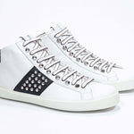 Tre quarti della parte anteriore del modello mid top bianco e nero sneaker. Tomaia in pelle con borchie, zip interna e suola in gomma bianca.