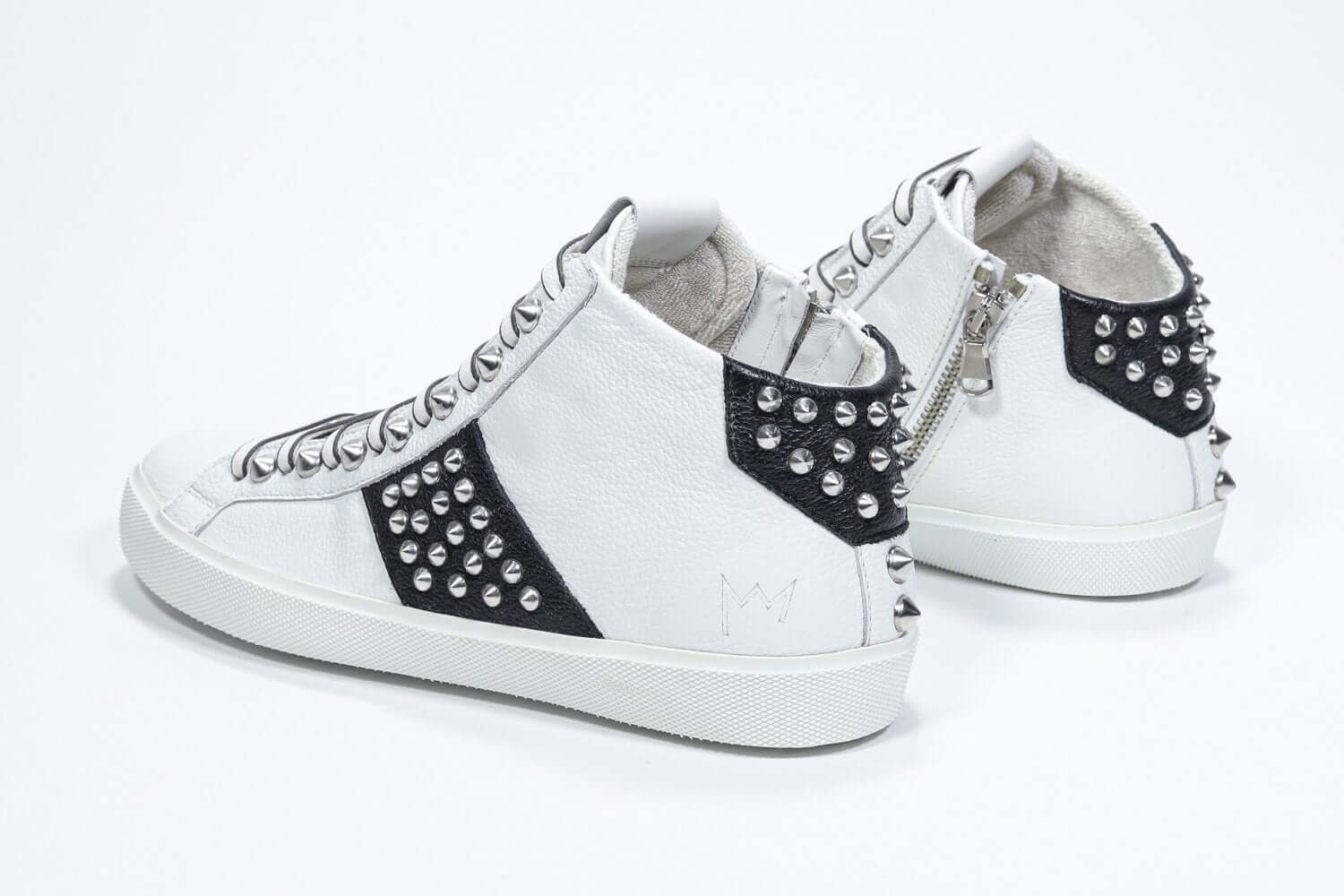 Vista posteriore a tre quarti del mid top bianco e nero sneaker. Tomaia in pelle con borchie, zip interna e suola in gomma bianca.