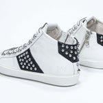 Vista posteriore a tre quarti del mid top bianco e nero sneaker. Tomaia in pelle con borchie, zip interna e suola in gomma bianca.