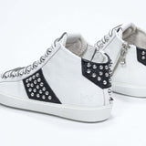 Vista posteriore a tre quarti del mid top bianco e nero sneaker. Tomaia in pelle con borchie, zip interna e suola in gomma bianca.