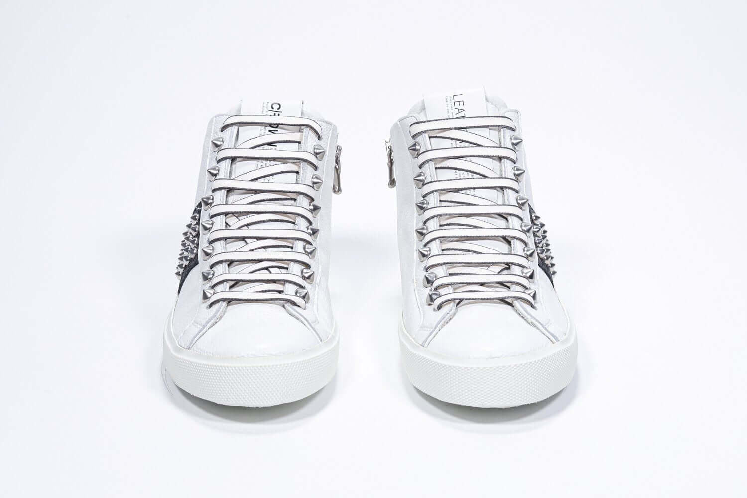 Vista frontale della mid top bianca e nera sneaker. Tomaia in pelle con borchie, zip interna e suola in gomma bianca.