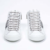 Vista frontale della mid top bianca e nera sneaker. Tomaia in pelle con borchie, zip interna e suola in gomma bianca.