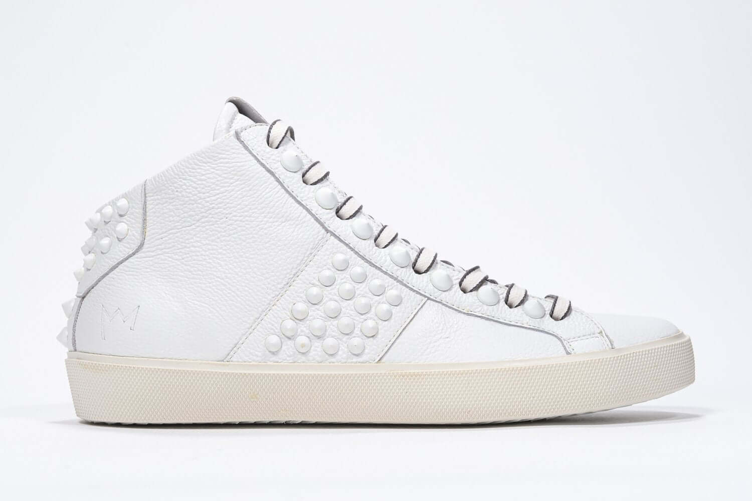 Side profile of mid top white sneaker. Full leather upper with studs, an internal zip and vintage rubber sole.