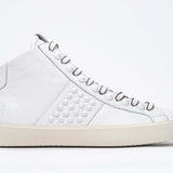 Side profile of mid top white sneaker. Full leather upper with studs, an internal zip and vintage rubber sole.