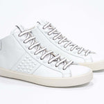 Three quarter front view of mid top white sneaker. Full leather upper with studs, an internal zip and vintage rubber sole.