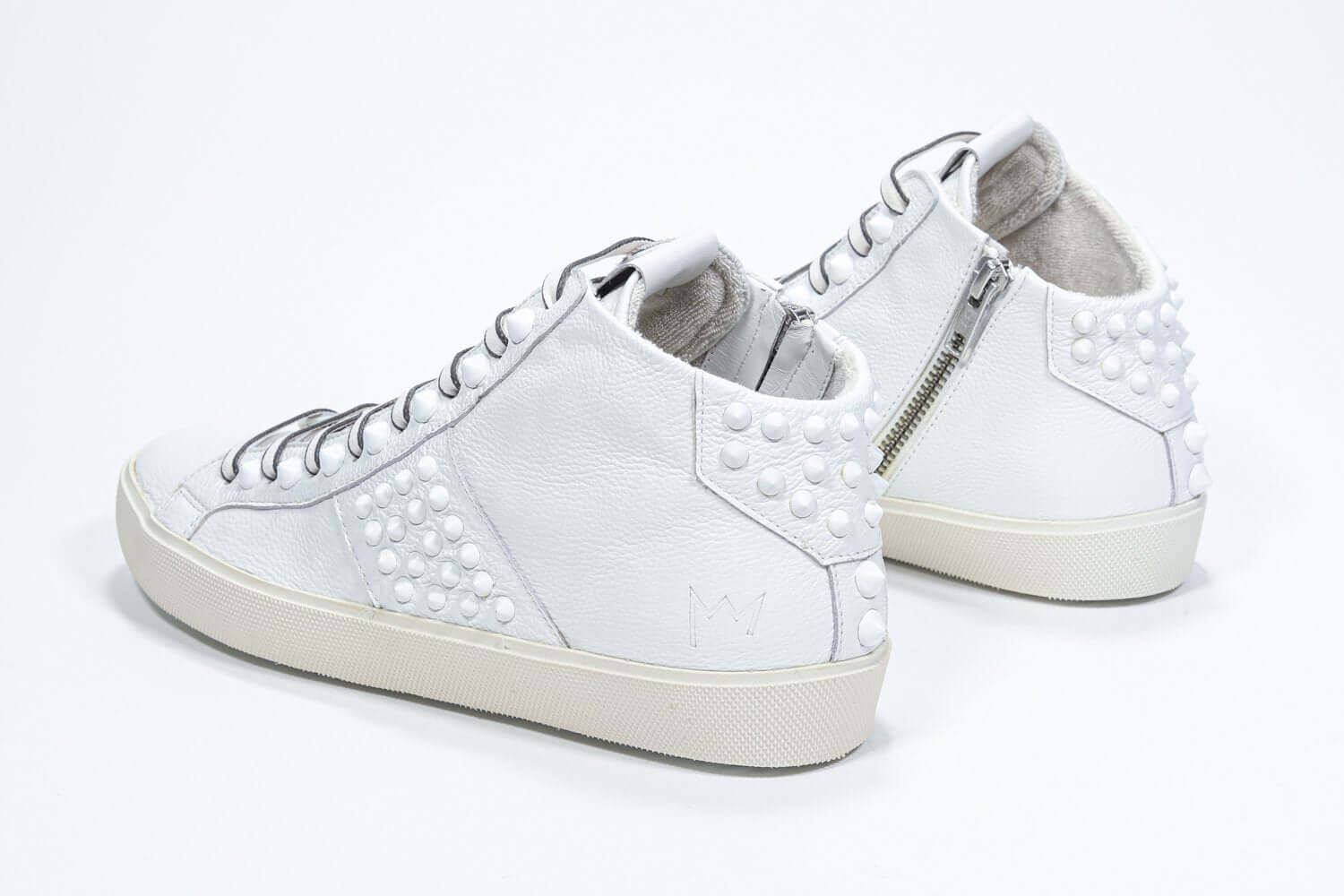 Three quarter back view of mid top white sneaker. Full leather upper with studs, an internal zip and vintage rubber sole.