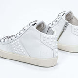 Three quarter back view of mid top white sneaker. Full leather upper with studs, an internal zip and vintage rubber sole.
