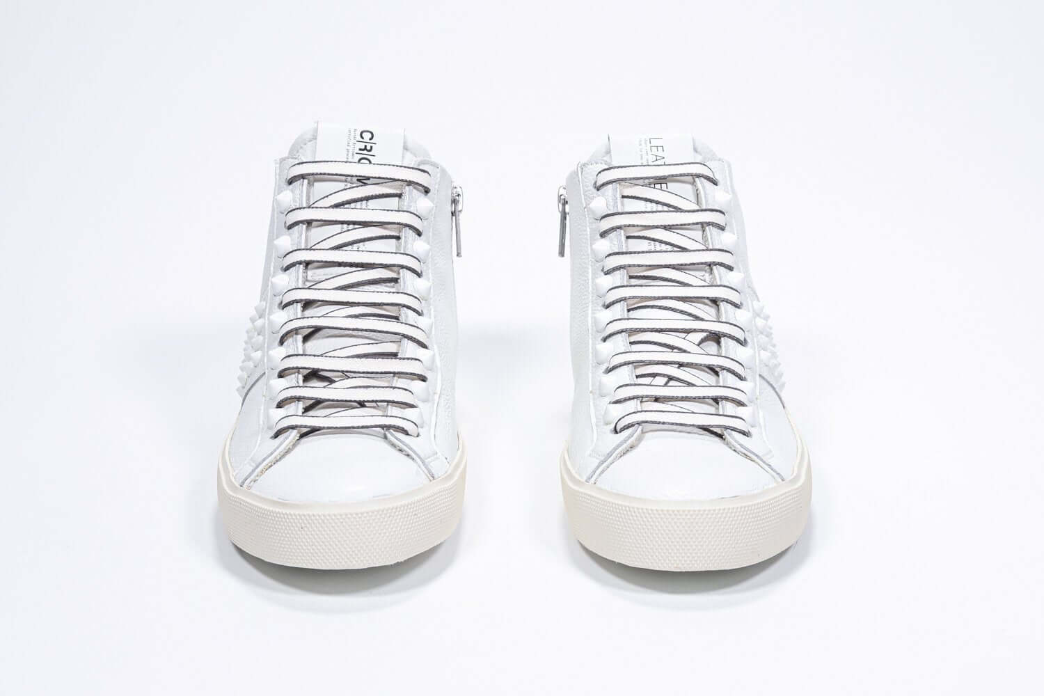 Front view of mid top white sneaker. Full leather upper with studs, an internal zip and vintage rubber sole.