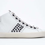 Side profile of mid top white sneaker. Full leather upper with studs, an internal zip and vintage rubber sole.