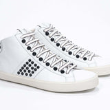 Three quarter front view of mid top white sneaker. Full leather upper with studs, an internal zip and vintage rubber sole.