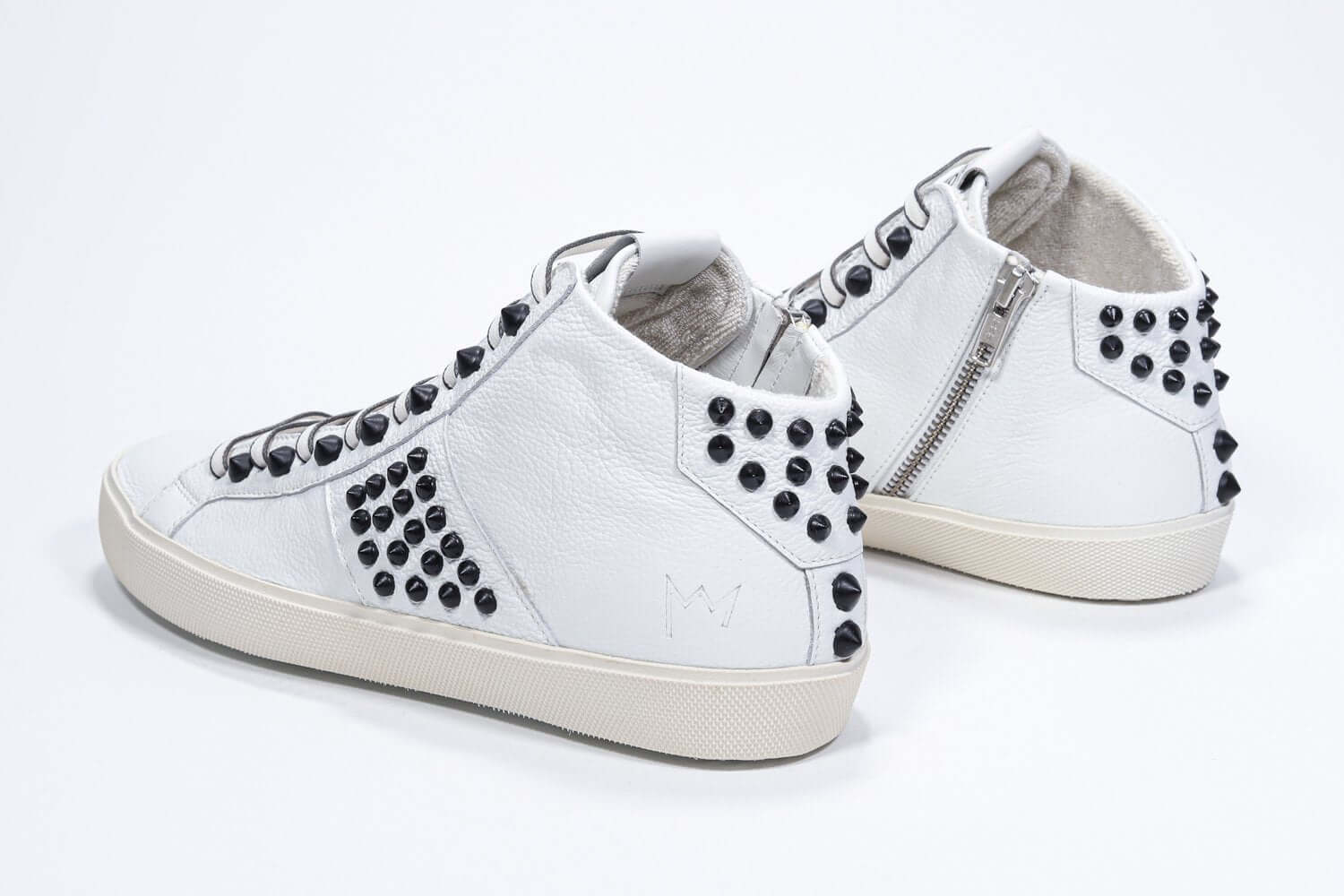 Three quarter back view of mid top white sneaker. Full leather upper with studs, an internal zip and vintage rubber sole.