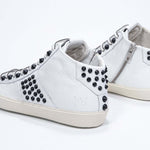 Three quarter back view of mid top white sneaker. Full leather upper with studs, an internal zip and vintage rubber sole.