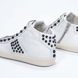 Three quarter back view of mid top white sneaker. Full leather upper with studs, an internal zip and vintage rubber sole.