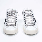 Front view of mid top white sneaker. Full leather upper with studs, an internal zip and vintage rubber sole.