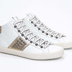 Vue de trois quarts avant d'un modèle intermédiaire blanc et or métallisé sneaker. Tige en cuir avec clous, fermeture à glissière interne et semelle en caoutchouc vintage.