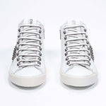 Vue de face d'un modèle intermédiaire blanc et or métallisé sneaker. Tige en cuir avec clous, fermeture à glissière intérieure et semelle en caoutchouc vintage.