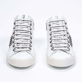 Vue de face d'un modèle intermédiaire blanc et or métallisé sneaker. Tige en cuir avec clous, fermeture à glissière intérieure et semelle en caoutchouc vintage.