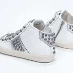 Dreiviertelansicht der Rückseite von Mid Top weiß und metallisch silber sneaker. Obermaterial aus Vollleder mit Nieten, internem Reißverschluss und Vintage-Gummisohle.