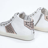 Vista posteriore di tre quarti di una mid top bianca e rosa metallizzata sneaker. Tomaia in pelle con borchie, zip interna e suola in gomma vintage.