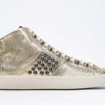 Profil latéral d'un modèle intermédiaire en or métallisé sneaker. Tige en cuir avec clous, fermeture éclair intérieure et semelle en caoutchouc vintage.