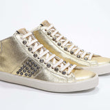 Vue de trois quarts avant d'un modèle intermédiaire en or métallisé sneaker. Tige en cuir avec clous, fermeture éclair intérieure et semelle en caoutchouc vintage.