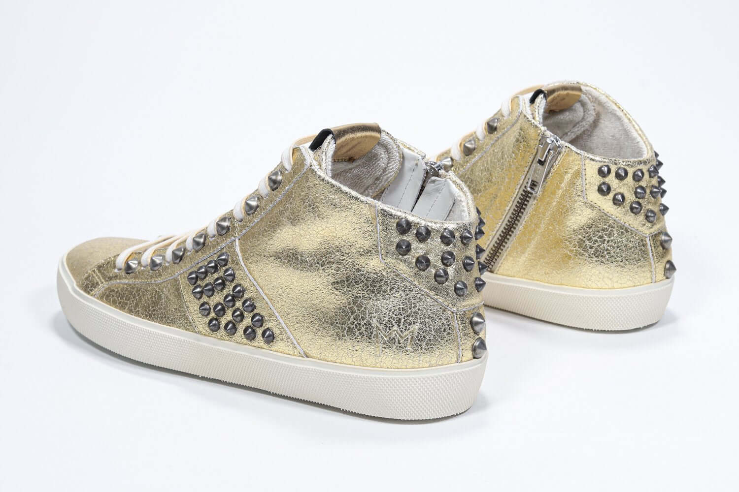 Vue de trois quarts arrière d'une chaussure de taille moyenne en or métallisé sneaker. Tige en cuir avec clous, fermeture éclair intérieure et semelle en caoutchouc vintage.