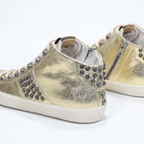 Vue de trois quarts arrière d'une chaussure de taille moyenne en or métallisé sneaker. Tige en cuir avec clous, fermeture éclair intérieure et semelle en caoutchouc vintage.