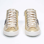 Vue de face de la chaussure intermédiaire en or métallisé sneaker. Tige en cuir avec clous, fermeture éclair intérieure et semelle en caoutchouc vintage.