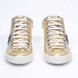 Vue de face de la chaussure intermédiaire en or métallisé sneaker. Tige en cuir avec clous, fermeture éclair intérieure et semelle en caoutchouc vintage.