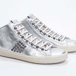 Dreiviertelansicht der Vorderseite von Mid Top Metallic Silber sneaker. Obermaterial aus Vollleder mit Nieten, einem internen Reißverschluss und einer Vintage-Gummisohle.