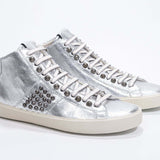 Dreiviertelansicht der Vorderseite von Mid Top Metallic Silber sneaker. Obermaterial aus Vollleder mit Nieten, einem internen Reißverschluss und einer Vintage-Gummisohle.