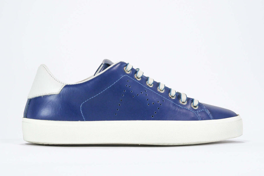 Side profile view of low top denim blue sneaker with white detailing and perforated crown logo on upper. Full leather upper and white rubber sole.