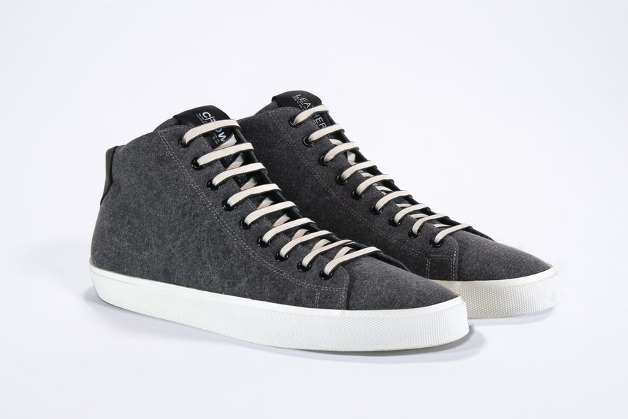 Three quarter front view of mid top sneaker in black canvas and leather upper, internal zip and white sole.