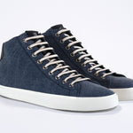 Three quarter front view of mid top sneaker in denim blue canvas and leather upper, internal zip and white sole.