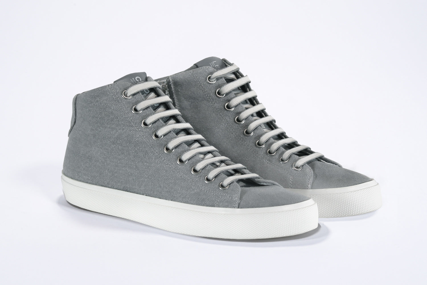 Vista frontale a tre quarti del modello mid top sneaker con tomaia in tela grigia, zip interna e suola bianca.