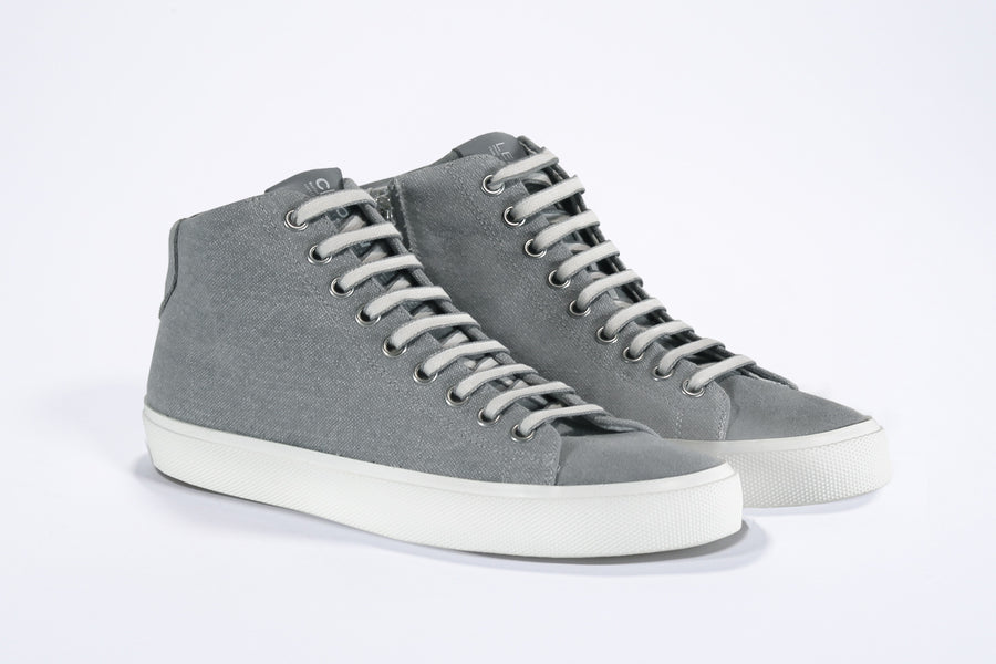 Three quarter front view of mid top sneaker with full grey canvas upper, internal zip and white sole.