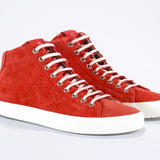 Three quarter front view of mid top sneaker in red suede and leather upper, internal zip and white sole.