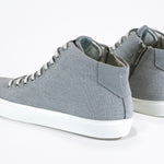 Three quarter back view of mid top sneaker with full grey canvas upper, internal zip and white sole.