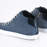 Three quarter back view of mid top sneaker in denim blue canvas and leather upper, internal zip and white sole.
