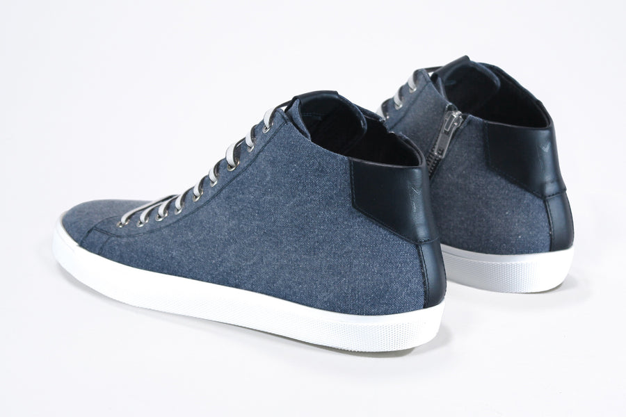 Three quarter back view of mid top sneaker in denim blue canvas and leather upper, internal zip and white sole.
