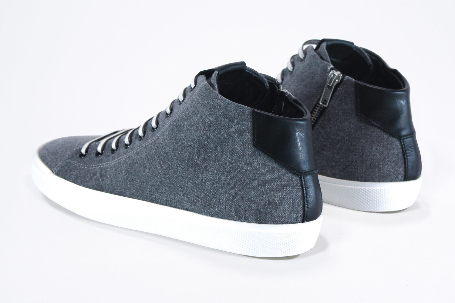 Three quarter back view of mid top sneaker in black canvas and leather upper, internal zip and white sole.