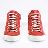 Front view of mid top sneaker in red suede and leather upper, internal zip and white sole.