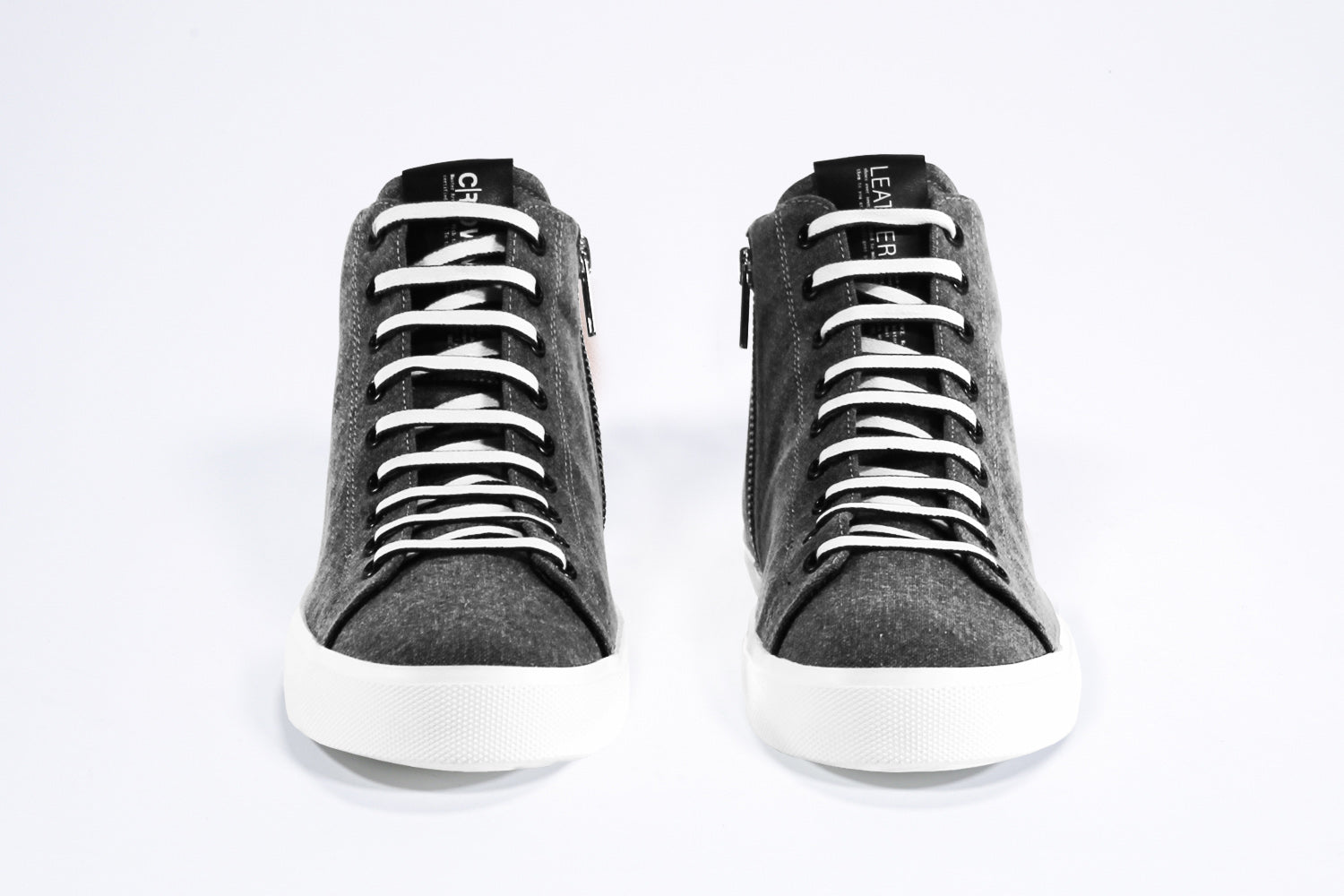 Vista frontale del modello mid top sneaker con tomaia in tela e pelle nera, zip interna e suola bianca.