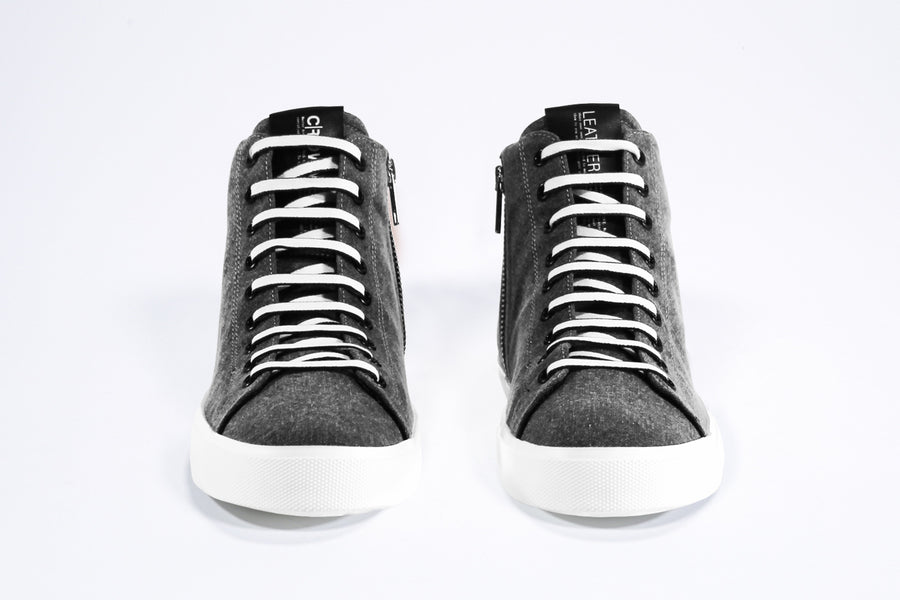 Front view of mid top sneaker in black canvas and leather upper, internal zip and white sole.