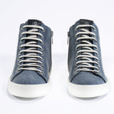 Vue de face du modèle mid top sneaker en toile bleu denim et tige en cuir, fermeture à glissière interne et semelle blanche.