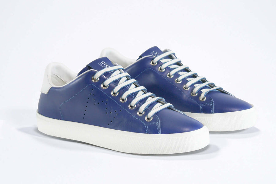 Three quarter front view of low top denim blue sneaker with white detailing and perforated crown logo on upper. Full leather upper and white rubber sole.