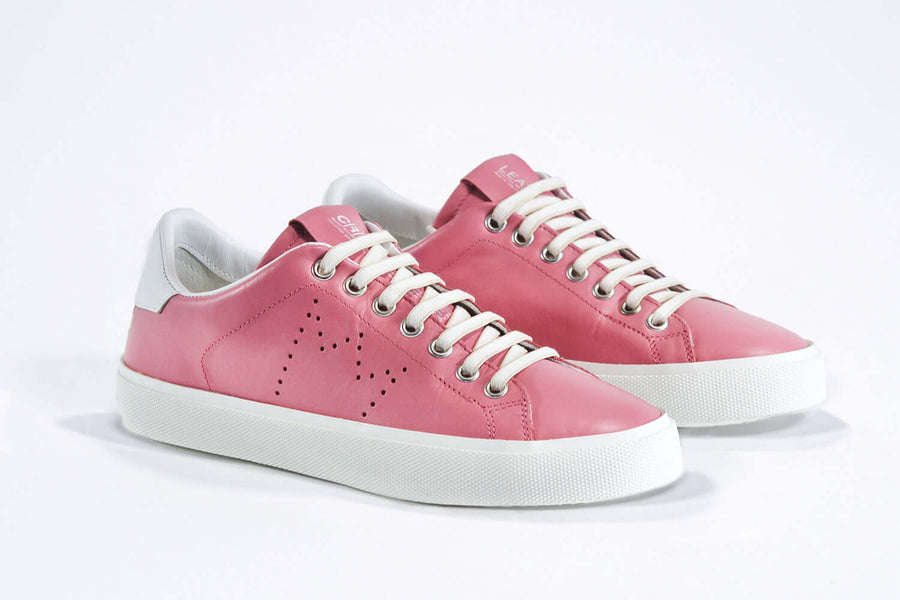  Three quarter front view of low top pink sneaker with white detailing and perforated crown logo on upper. Full leather upper and white rubber sole.